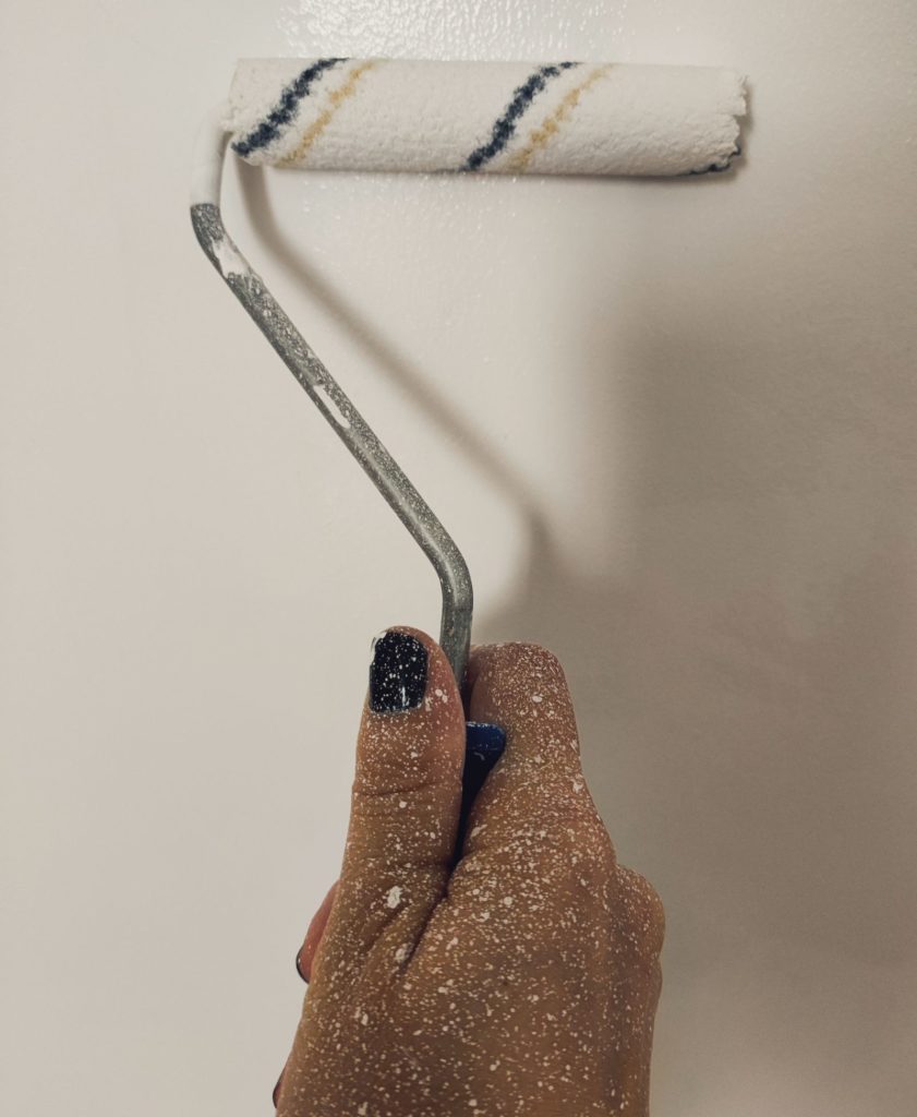 Hand holding a paint roller against a wall