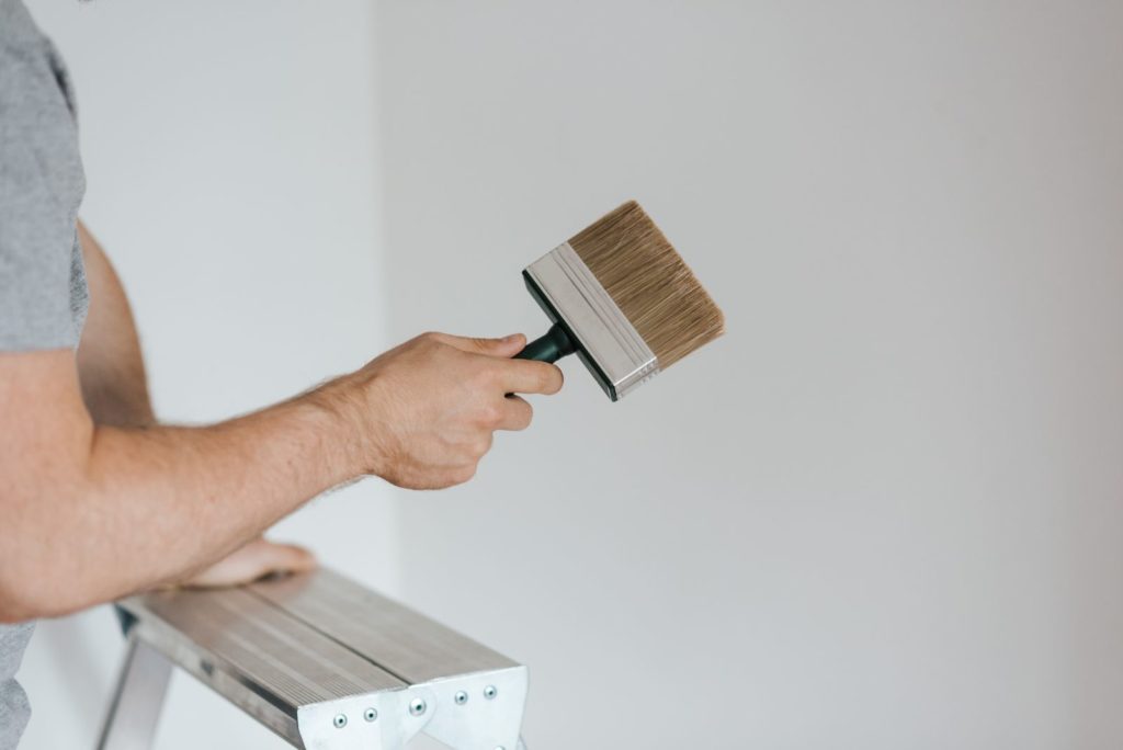 Hand holding a paintbrush next to a ladder